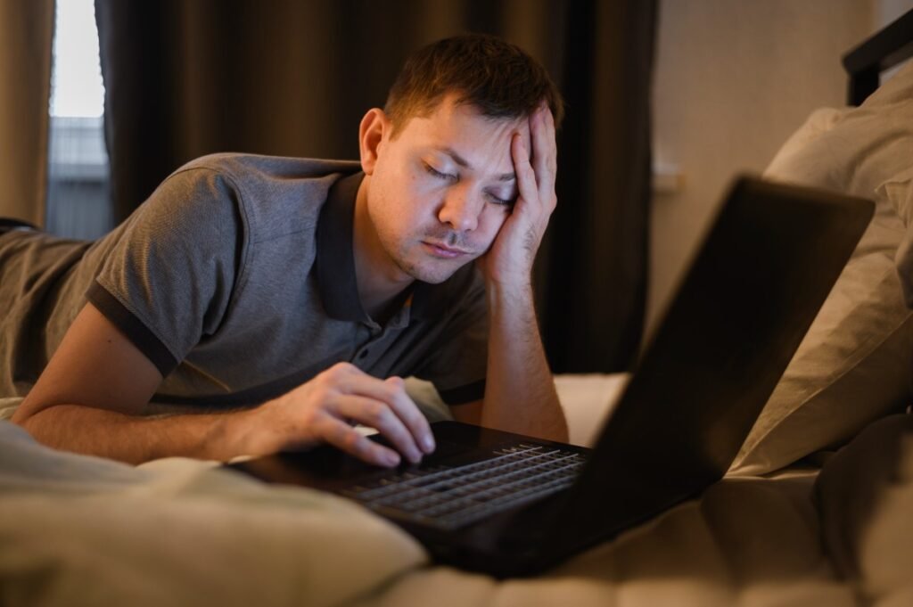 Tired person using a laptop in bed.