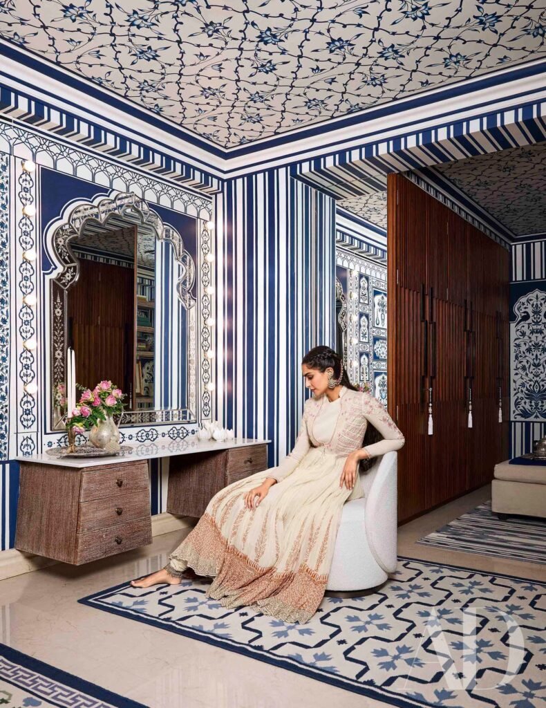 Elegant blue-and-white patterned room with a woman seated beside a decorative mirror and wooden cabinet.