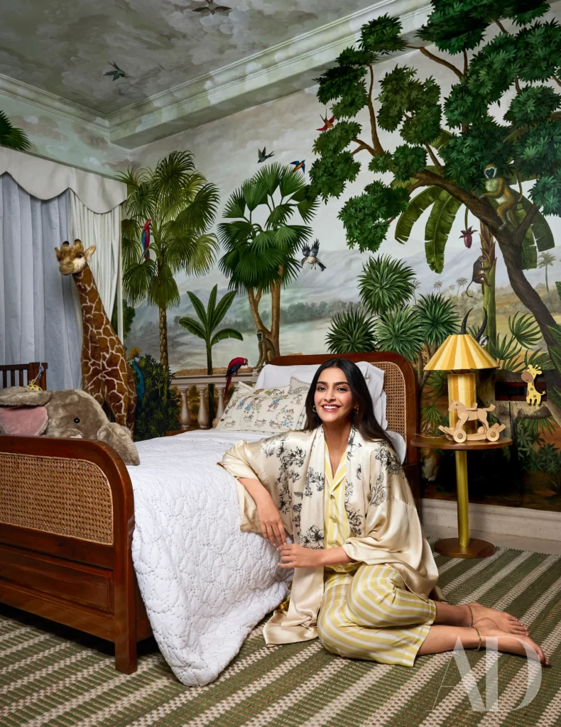 A smiling woman in pajamas sits beside a bed in a jungle-themed bedroom with animal decor.