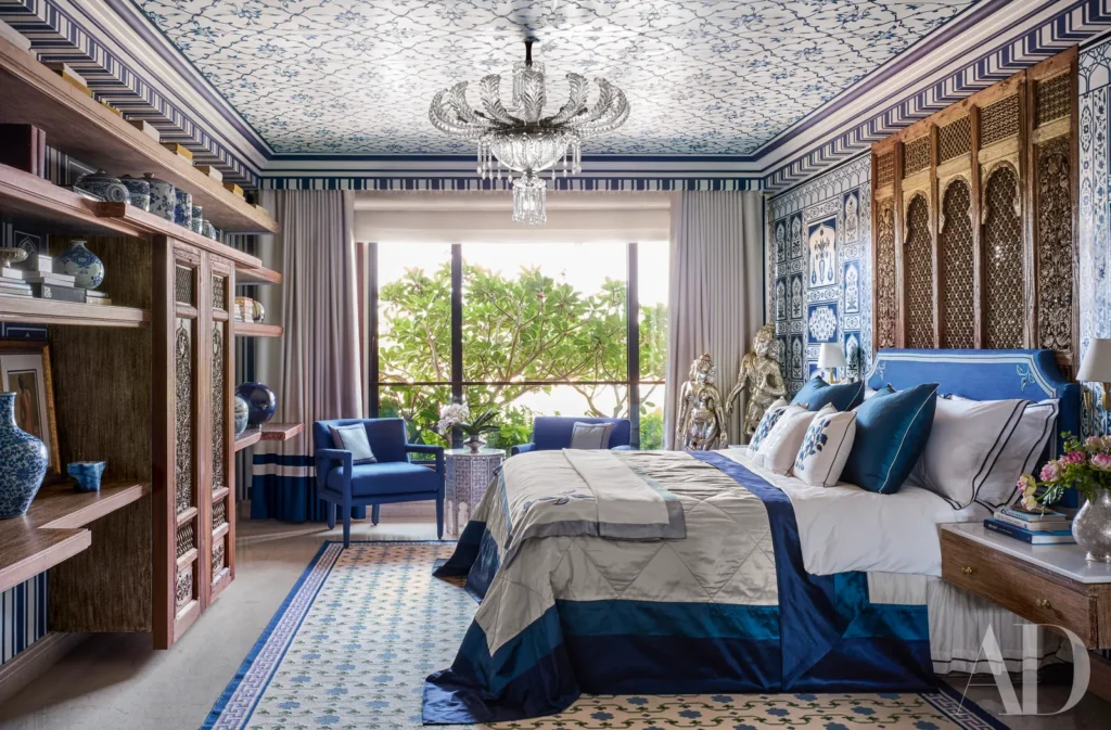 Luxury blue-and-white bedroom with patterned walls, a decorative ceiling, chandelier, and large window.