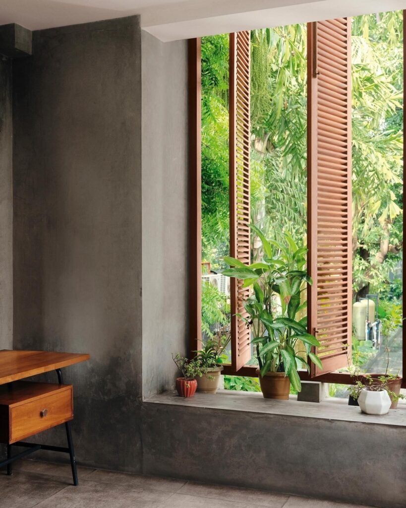 Anamika Khanna-inspired interior with wooden shutters, indoor plants, and a minimalist desk beside a lush garden view.