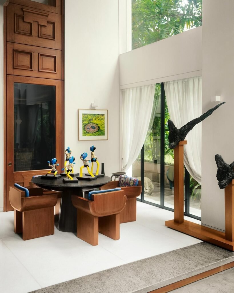 Anamika Khanna-inspired interior with wooden furniture, colorful sculptures, artwork, and large glass windows.