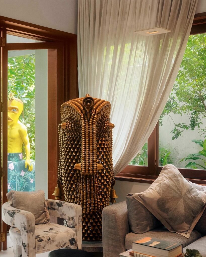 Anamika Khanna-inspired interior featuring a sculptural woven artwork, cozy seating, and sheer curtains overlooking greenery.