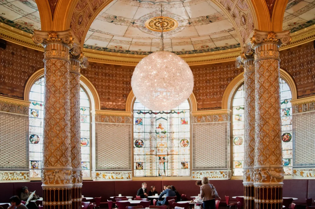 Elegant historic interior with ornate columns, stained-glass windows, and a large chandelier.
