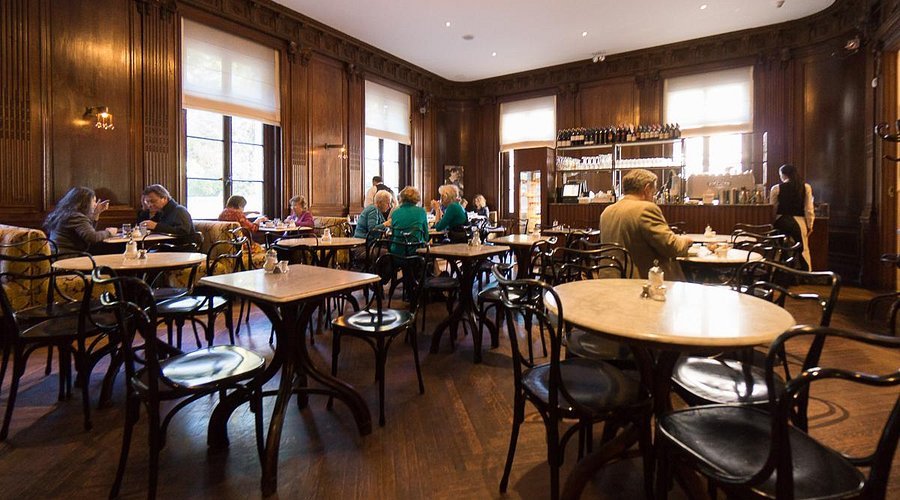 Elegant wood-paneled café with patrons seated at small tables.
