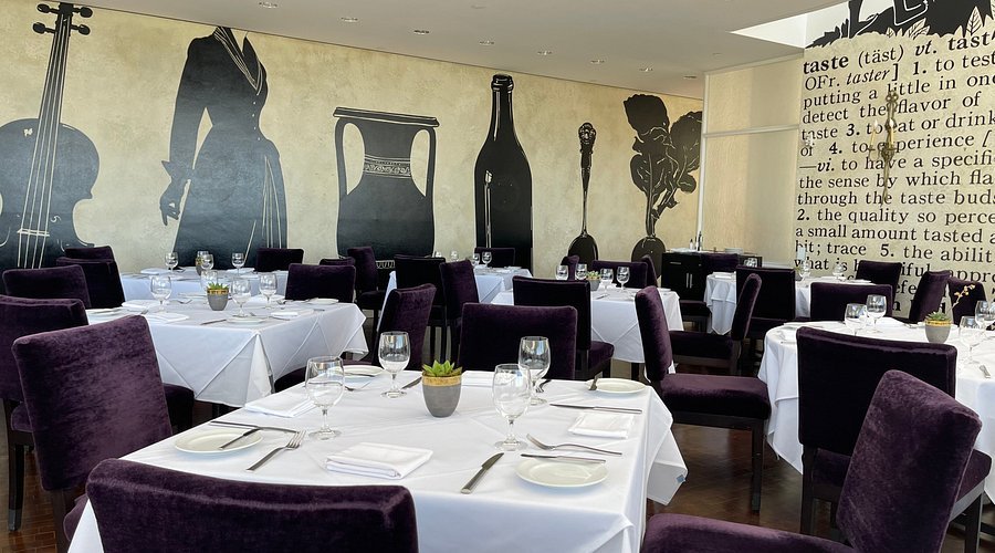 Elegant restaurant dining room with white tablecloths, purple chairs, and a large food-and-drink mural.