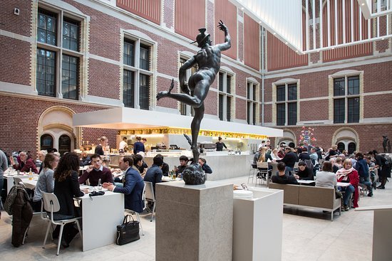 Museum courtyard with a bronze sculpture, café seating, and visitors dining inside a historic brick building.