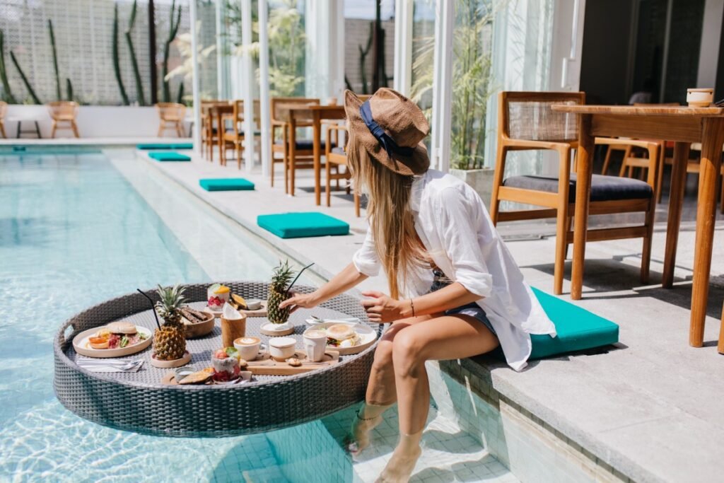 Woman relaxing by a resort pool with breakfast and tropical fruit on a floating tray.